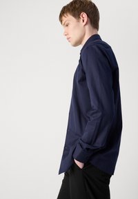 Navy long-sleeve shirt made of textured fabric with a herringbone pattern, featuring a buttoned collar and cuffs, paired with black pants.