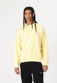 Yellow sweatshirt with a crew neck, soft texture, and green logo detail. Paired with black cargo pants featuring side pockets.