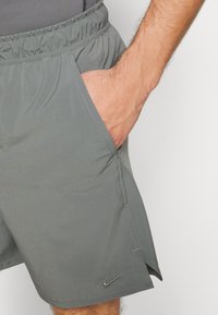 Calções atléticos cinzentos com uma cintura elástica, bolsos laterais e um pequeno logótipo preto da Nike perto da bainha. Tecido suave e leve.