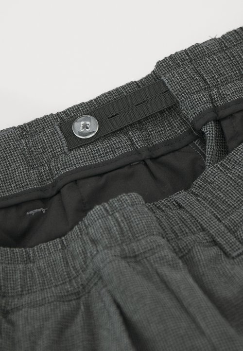 Pantalones cortos de cuadro gris con cintura elástica, cierre de botón y un forro interior suave. Detalles cosidos a lo largo de los bordes.