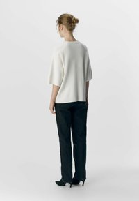 Haut blanc ample à manches courtes, en maille texturée, associé à un jean foncé et des talons aiguilles, vu de dos.