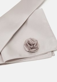 Helles graues Herrenhemd mit ribbeliger Textur, versehen mit einem runden, gefalteten Stoffakzent, der einer Blume ähnelt. Glatte Oberfläche mit detaillierter Naht.