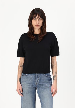 Svart kortermet strikket topp med rund hals, kombinert med lyseblå jeans med dekorative detaljer på fronten.