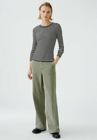 Un haut à rayures noires et blanches à manches longues associé à un pantalon large vert olive. La tenue présente une silhouette ajustée et une texture décontractée.