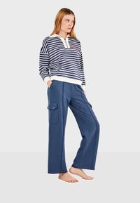 Mornarsko plava i bijela prugasta majica dugih rukava s kragnom i prednjim džepom, u kombinaciji s labavim mornarsko plavim cargo hlačama koje imaju bočne džepove.