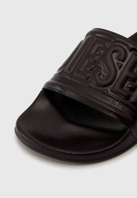 Black slide sandal featuring a textured upper, embossed branding, and a smooth, rounded footbed. Durable material with a minimalist design.