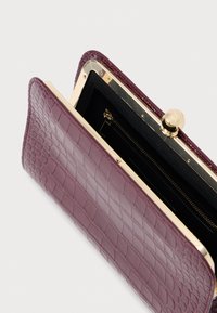 Τσάντα από δέρμα σε μπορντό απόχρωση με ανάγλυφο σχέδιο κροκολόφου και χρυσό κούμπωμα, καθώς και εσωτερική τσέπη με φερμουάρ. Ραφές στο εξωτερικό με λείες εσωτερικές επενδύσεις.