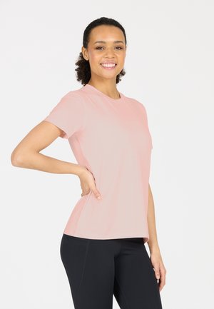 T-shirt rose clair à manches courtes avec col rond, fabriqué dans un matériau lisse et extensible. Design ajusté, porté avec des leggings noirs.