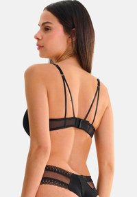 Ensemble de lingerie noire comprenant un soutien-gorge en maille avec bretelles réglables et fermeture à crochets. Le string assorti présente des accents en dentelle le long de la taille.