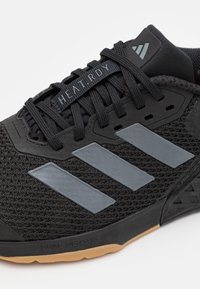 Scarpa sportiva nera con tomaia in rete, presenta tre strisce grigie, etichetta HEAT.RDY e suola in gomma con accenti a motivo per una migliore presa.