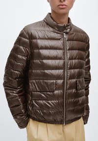 Veste matelassée marron avec une finition brillante, col haut, fermeture éclair avant et deux poches plaquées. Comprend des panneaux matelassés horizontaux et un ourlet élastique.