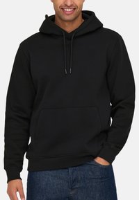 Hoodie noir avec une poche kangourou, un cordon de serrage ajustable et des poignets côtelés. Fabriqué à partir d'un tissu solide et doux.