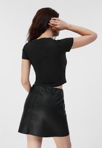 Black cropped t-shirt made of soft fabric paired with a black faux leather mini skirt. The skirt features a waistband and subtle stitching details.