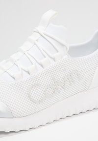 Vita mesh-sneakers med texturerad yta, gummisulor och elastiska snören. Har präglad "Calvin"-logotyp på sidan.