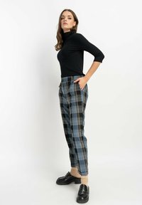 Czarny sweter z golfem, spodnie w kratkę w odcieniach niebieskiego, czarnego i szarego. Spodnie mają boczne kieszenie i luźny krój. Założone czarne mokasyny.