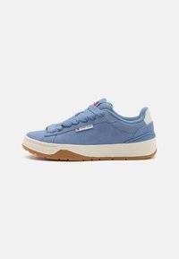 Baskets en suede bleu clair avec des lacets texturés, semelle intermédiaire blanche et semelle extérieure en caoutchouc brun. Présente un patch logo sur le côté.