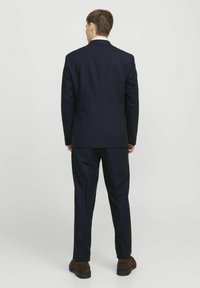 Tumes sinna ja püksid kitseprooviga, pehme kangaga ja sirge selja disainiga, koos pruuni nahast kingadega.