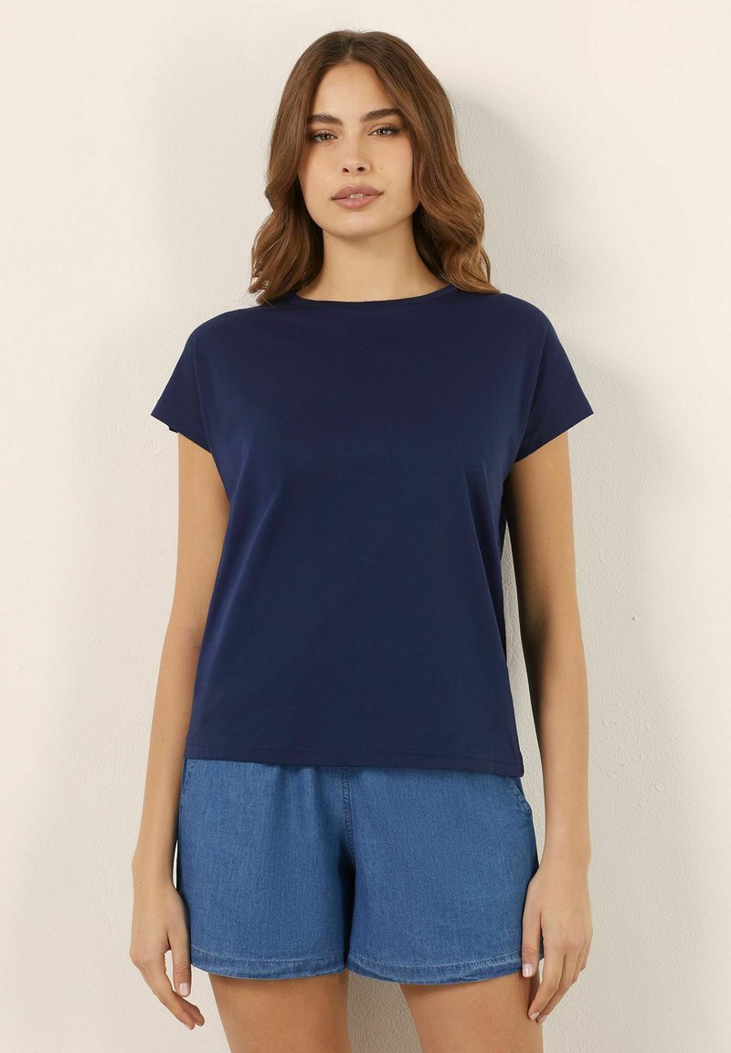 Mörkblå kortärmad t-shirt med rund halsringning, tillverkad av mjukt tyg. Kombinerad med ljusa denimshorts med elastisk midja.