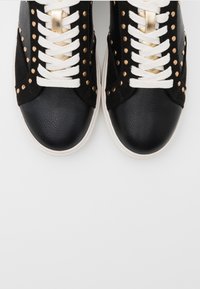 Svarta och vita sneakers med en strukturerad ovansida, gyllene dekorativa nitar och tjocka vita snören med en rund tådesign och gummisula.