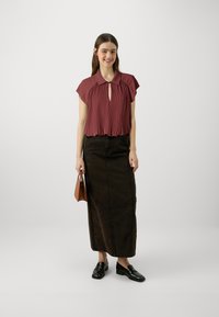 Maroon pleated blouse with short sleeves and a keyhole detail, paired with a long dark brown denim skirt and black loafers. Brown handbag.