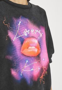 Sudadera negra con un gráfico colorido de labios y rayos, con las palabras "Lover" y "Kiss" en blanco brillante y rosa neón.