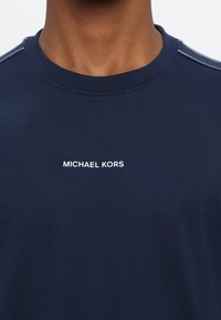 Sötétkék pamut póló kerek nyakkivágással, fehér "MICHAEL KORS" logóval az elején és finom vállvarrás részletekkel.