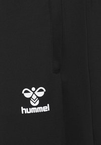 Black fabric with a white stylized bee logo and the text "hummel" printed beneath it on a garment.