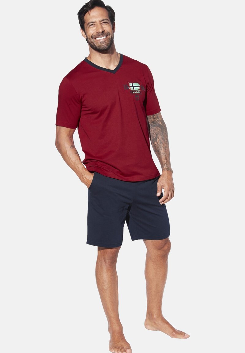 Red V-neck shirt with a pocket detail and logo, paired with navy shorts. Smooth fabric, casual fit, and short sleeves.