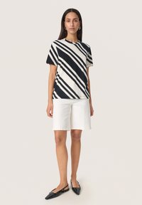 Sort og hvid stribet bomulds t-shirt med korte ærmer, parret med hvide shorts til knæene og sorte spidse fladsko.