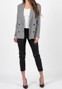 Blazer double boutonnage en noir et blanc à motif pied-de-poule avec revers pointus, associé à un pantalon en simili cuir noir ajusté et des talons noirs pointus.