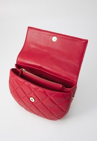 Röd quiltad läderhandväska med guldfärgade detaljer, som har ett magnetiskt knäppstängning och en innerficka med dragkedja. Slät yta och rundad form.
