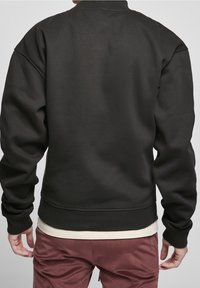 Sudadera negra con cuello redondo, puños y dobladillo acanalados. Hecha de una tela suave, con una textura lisa y un corte relajado.