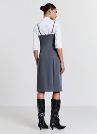 Graues Kleid mit verstellbaren Spaghettiträgern und einer strukturierten Silhouette, kombiniert mit glänzenden schwarzen kniehohen Stiefeln. Glatte Stoffstruktur.