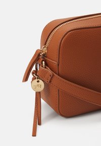 Brown leather bag with a textured finish, gold zipper, and charm. Features a detachable strap and rounded edges for a compact shape.