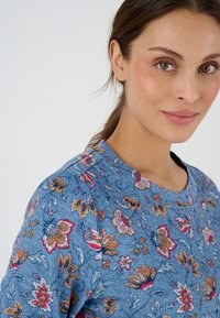 Top blu con motivo floreale, dotato di scollatura rotonda e maniche corte, realizzato in tessuto testurizzato con accenti floreali colorati.