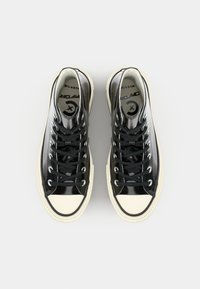 Svarte patent høye sneakers med hvite gummitær, svarte lisser og avrundet form. Har logo på sålen og glatt tekstur.