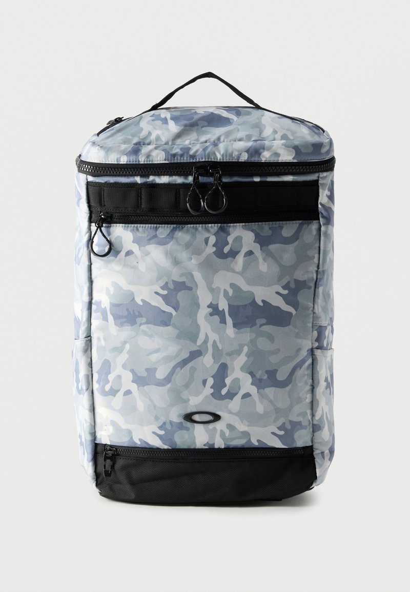 Ορθογώνιο σακίδιο με ανοιχτό γκρι και μπλε καμουφλάζ σχέδιο, μαύρο κάτω μέρος, εμπρόσθιες τσέπες με φερμουάρ και χειρολαβή στην κορυφή.