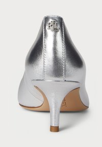 Silver metallic high-heeled shoe with a textured finish, pointed toe, and a small logo on the back heel. Features a slender stiletto heel.