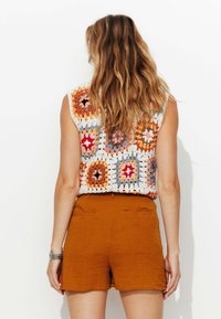 Top au crochet composé de patches hexagonaux colorés en orange, rose et bleu, associé à un short texturé de couleur rouille.