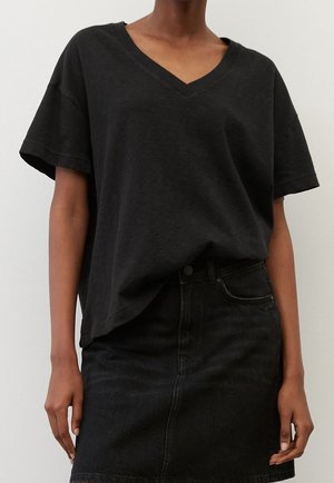 Person wearing a loose black V-neck short sleeve shirt tucked into a high-waisted black denim skirt against a plain light background.