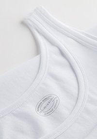 Witte katoenen tanktop met een ronde halslijn, voorzien van een gestikt afwerking. Het label leest "Superieure Kwaliteit Infimissimi Surima Katoen."