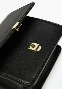 Schwarzleder Handtasche mit einem goldfarbenen Schlossverschluss. Das Innere ist geräumig, mit einer glatten Textur und klaren Linien.