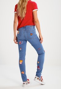 Ljusblå denimjeans med flera färgglada livsmedelsinspirerade broderade lappar, figursydd design och råa fållar. Matchas med vita sneakers.