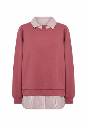 Pikkade varrukatega tuhmunud roosa pusa, mille all on valge särk punaste õhukeste vertikaalsete triipudega krae ja äärel.