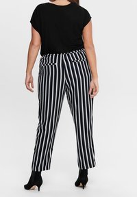 Svart kortärmad topp i kombination med marinblå och vitrandiga högmidjade byxor med framfickor och ankellång längd. Kompletterad med klackar.