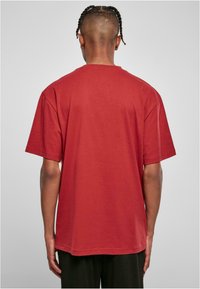 Tricou din bumbac roșu, cu croială lejeră, mâneci scurte și decolteu rotund, expus din spate pe un fundal gri deschis.