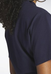 Námořnická modrá bavlněná tričko s krátkými rukávy, s kulatým výstřihem a měkkou texturou. Tkanina se jeví jako hladká s minimem švů.