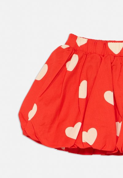 Rødt innsamlet skjørt med elastisk midjebånd og hvite hjerte mønstre spredt over stoffet på lys bakgrunn.