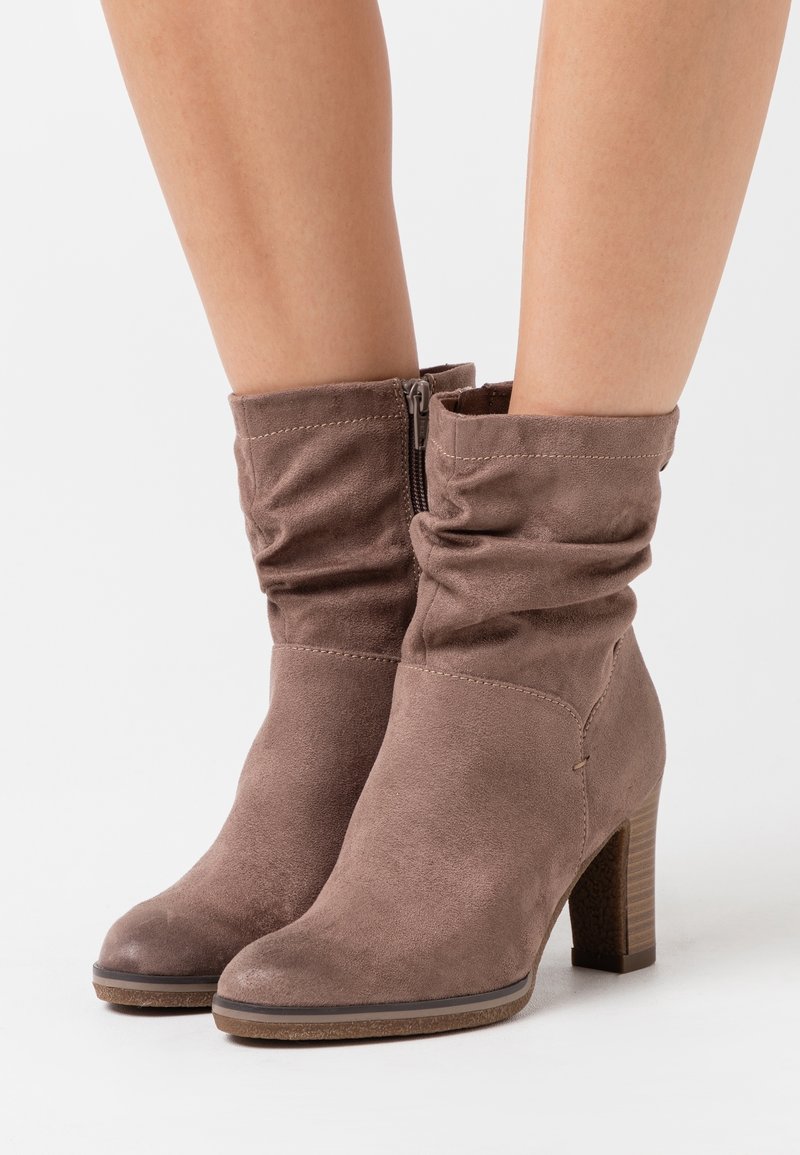 Bottines en daim marron avec un dessus froncé, une fermeture éclair latérale et un talon empilé, présentant une texture lisse et un design d'orteil arrondi.