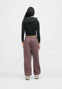 Juodas trumpas sukapotas džemperis su gaubtu, derinamas su laisvomis mauve spalvos treningo kelnių. Džemperis turi ilgas rankoves, o kelnes laiko elastinga juosta.